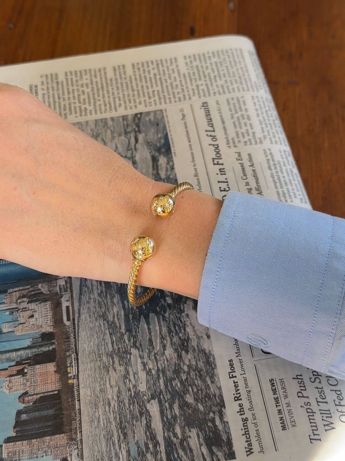 Gold bracelet on a wrist with a newspaper background