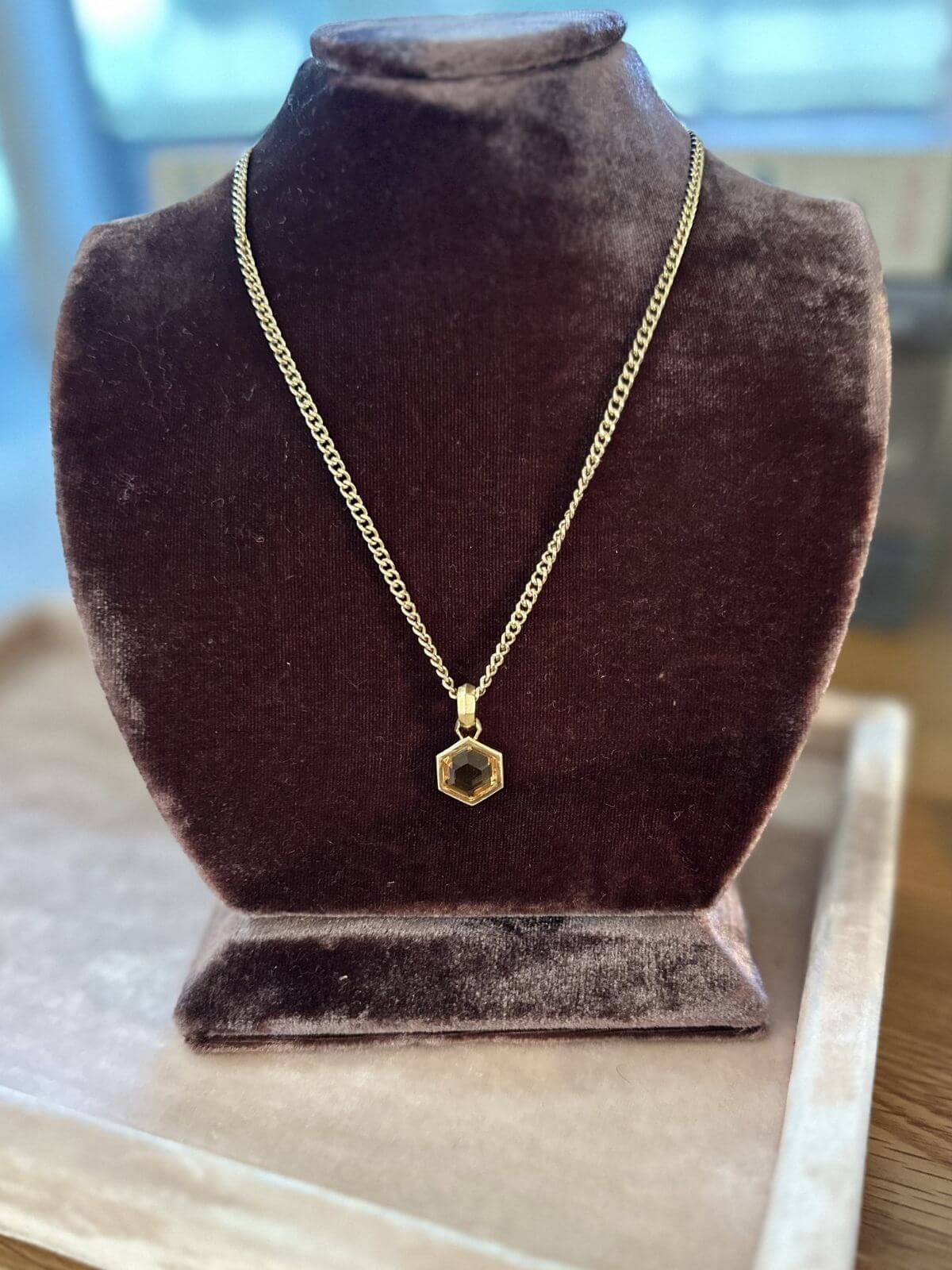 David Yurman Gold necklace with a hexagonal pendant on a pink fixture and brown neckform