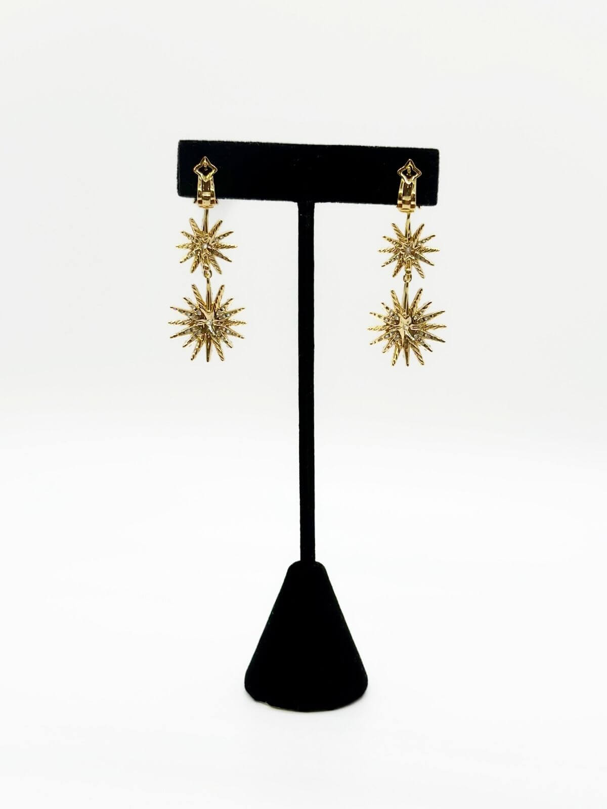 Gold star-shaped earrings on a black earring stand against a white background