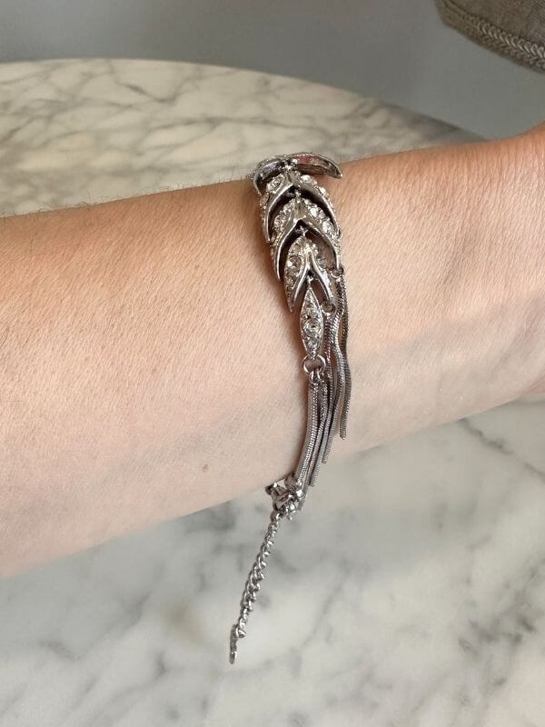 Louise Row Studio featuring Dior silver feather inspired bracelet made of silver and crystals on arm with marble table below. 
