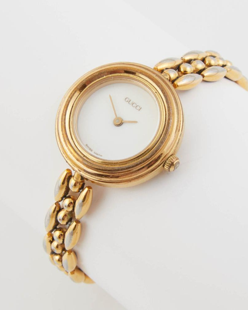 Gold Gucci watch with a white face on a light gray background