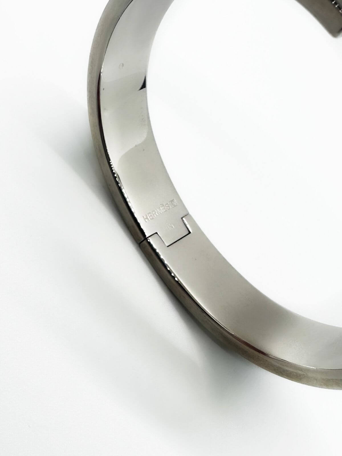 Hermes Clic H bracelet in stainless steel and black enamel on white background. 