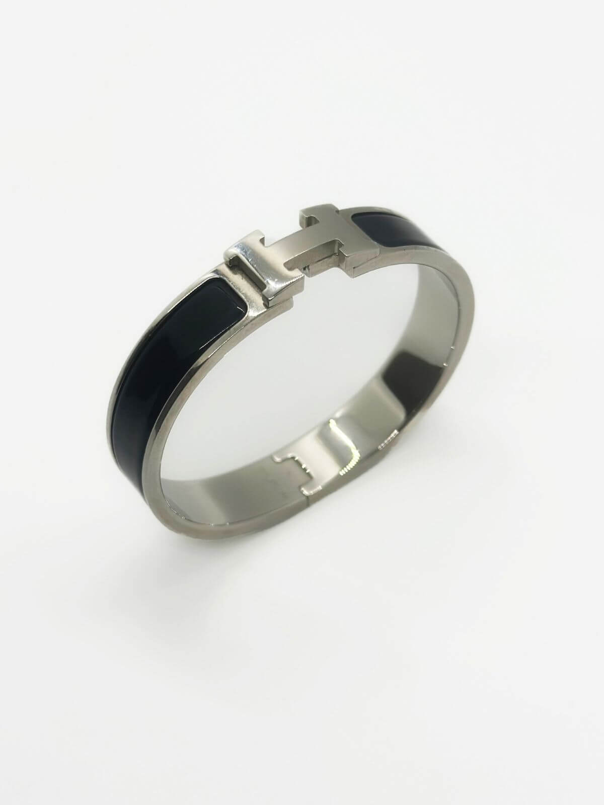 Hermes Clic H bracelet in stainless steel and black enamel on white background. 