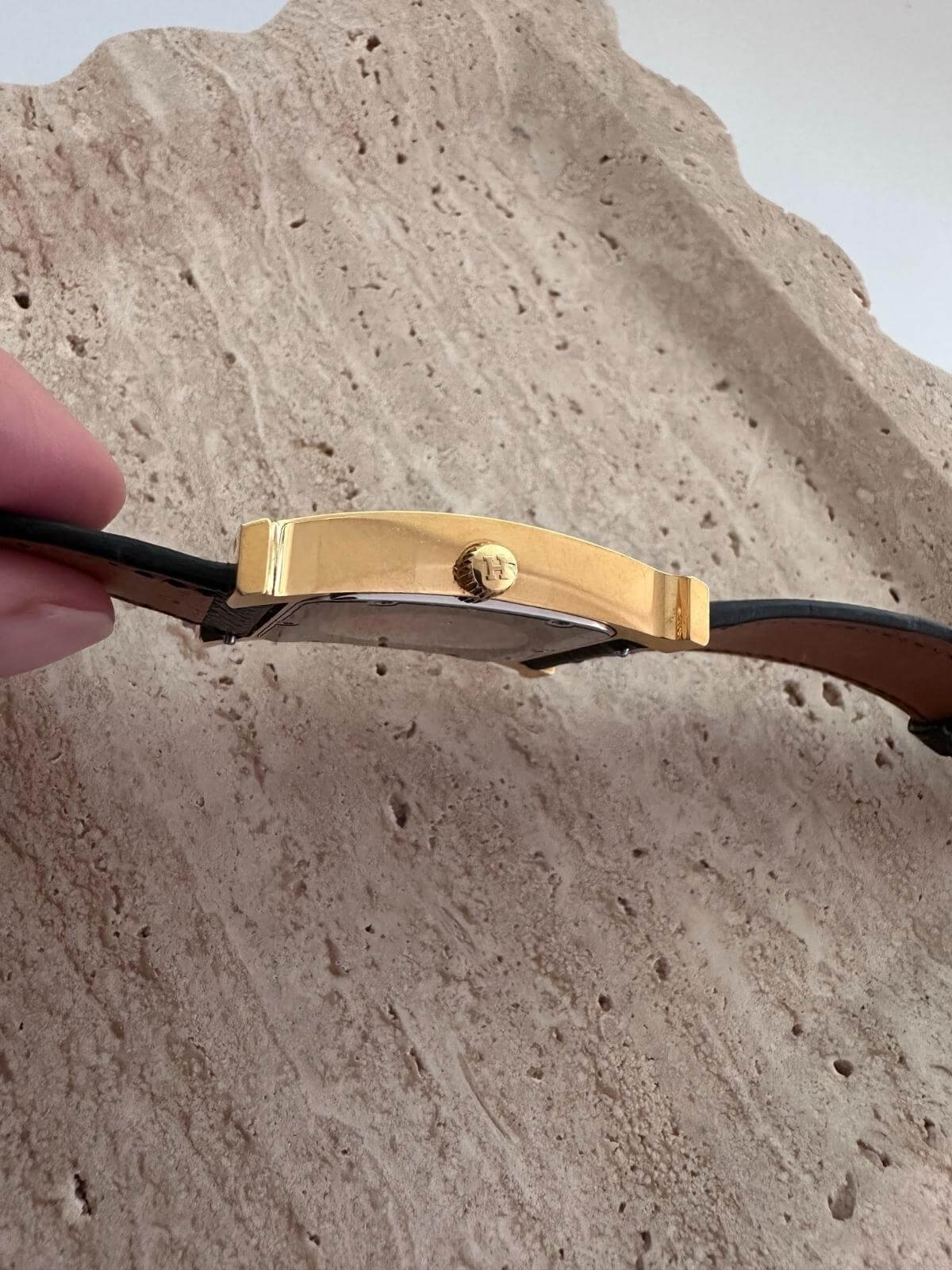 Side of Hermes Gold watch band held against a rocky background