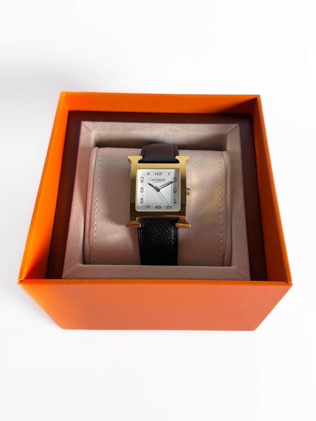 Hermes Watch with black strap and gold case in an orange box on a white background