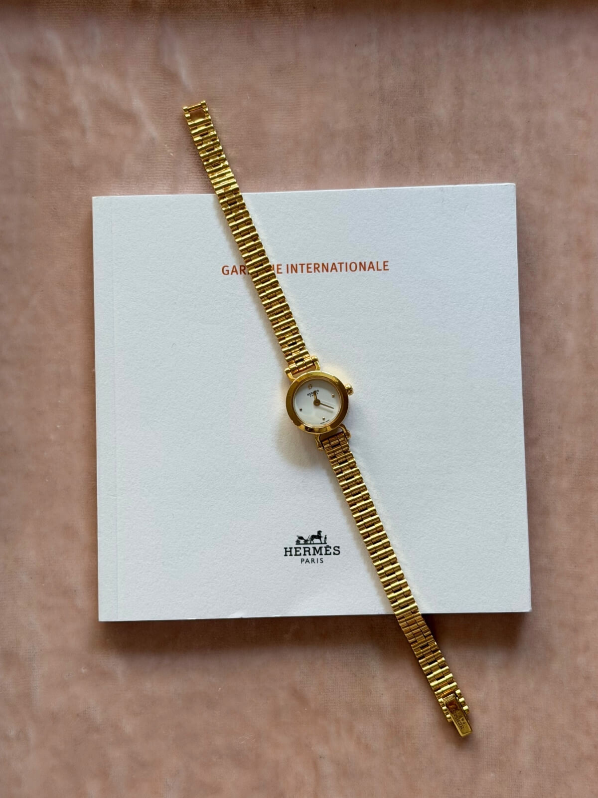 Louise Row featuring Hermes 18K yellow gold Faubourg watch on pink tray over warranty card