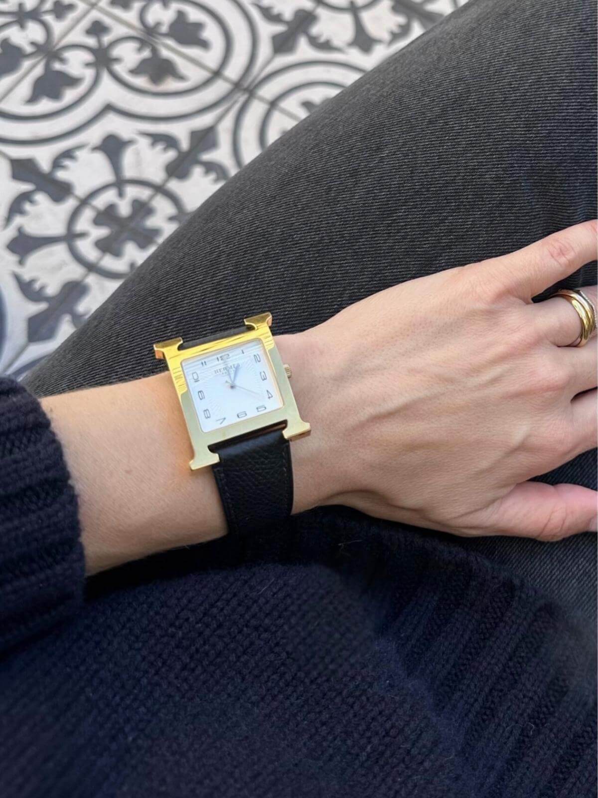 Model wearing Hermes H Heure gold watch on jeans with pattern background