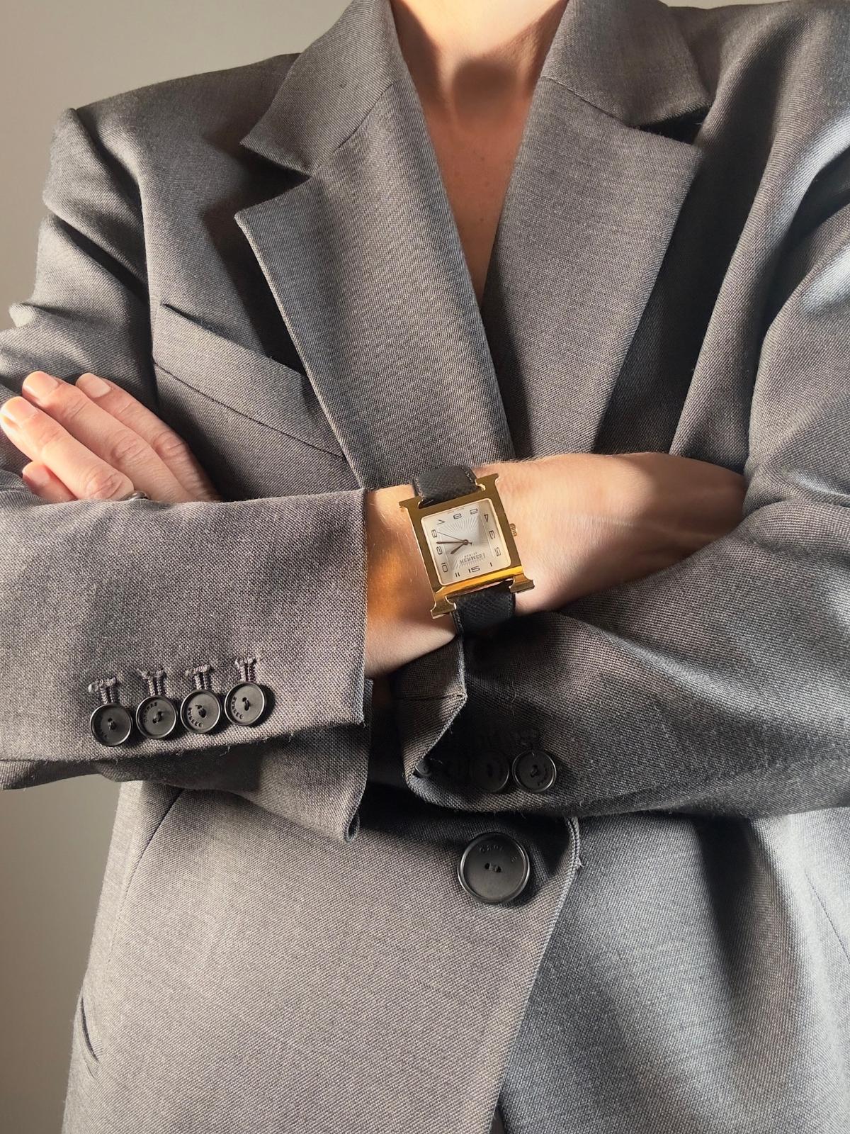 Person wearing a gray suit with a hermes gold watch on a neutral background