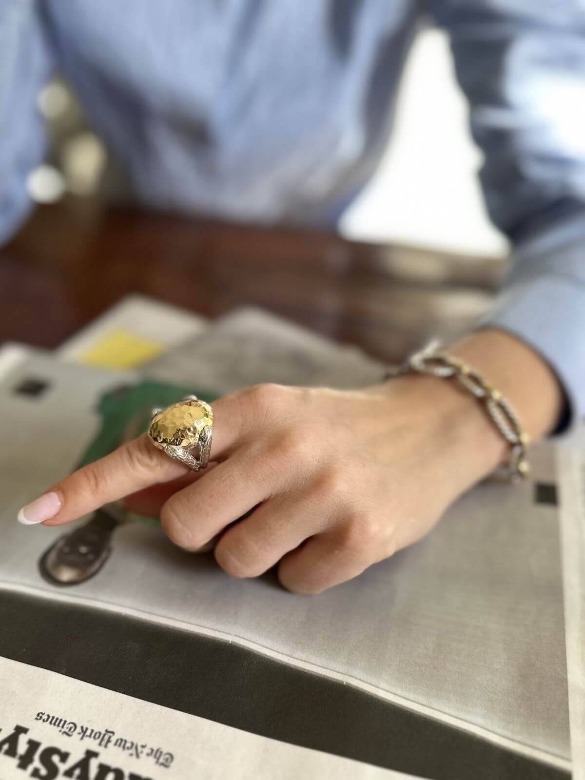 Close-up of a hand wearing a gold ring on a metallic surface with a blurred background