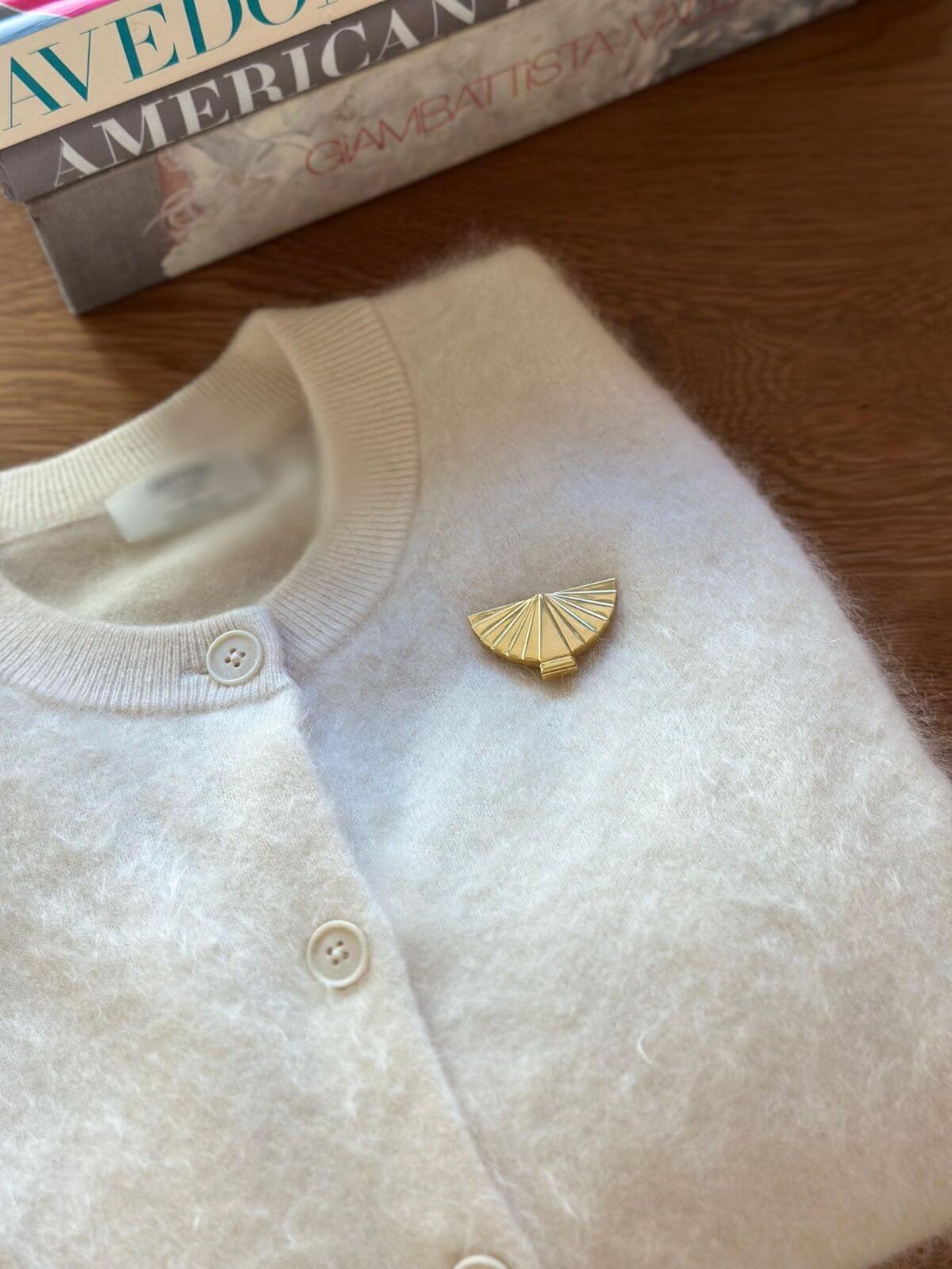 Louise Row Studio vintage Karl Lagerfeld gold fan brooch on white folded cardigan. 