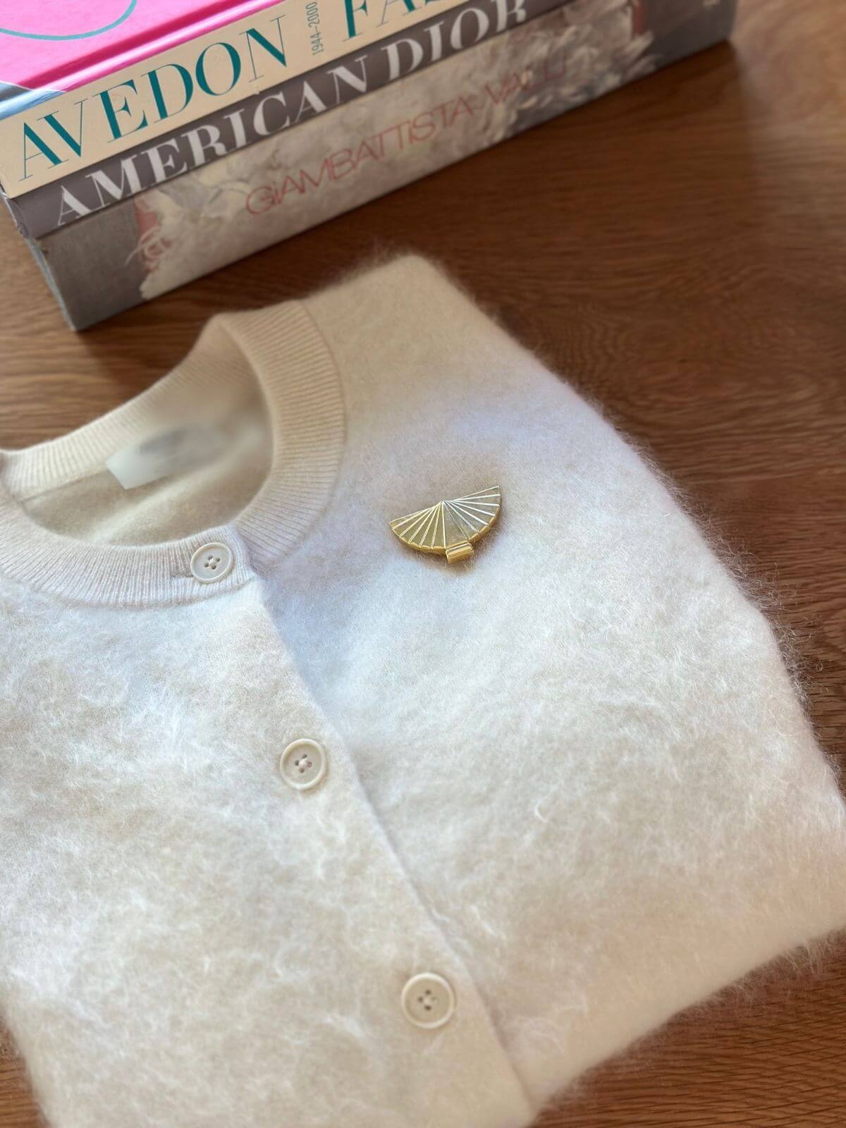 Louise Row Studio vintage Karl Lagerfeld gold fan brooch on white folded cardigan. 