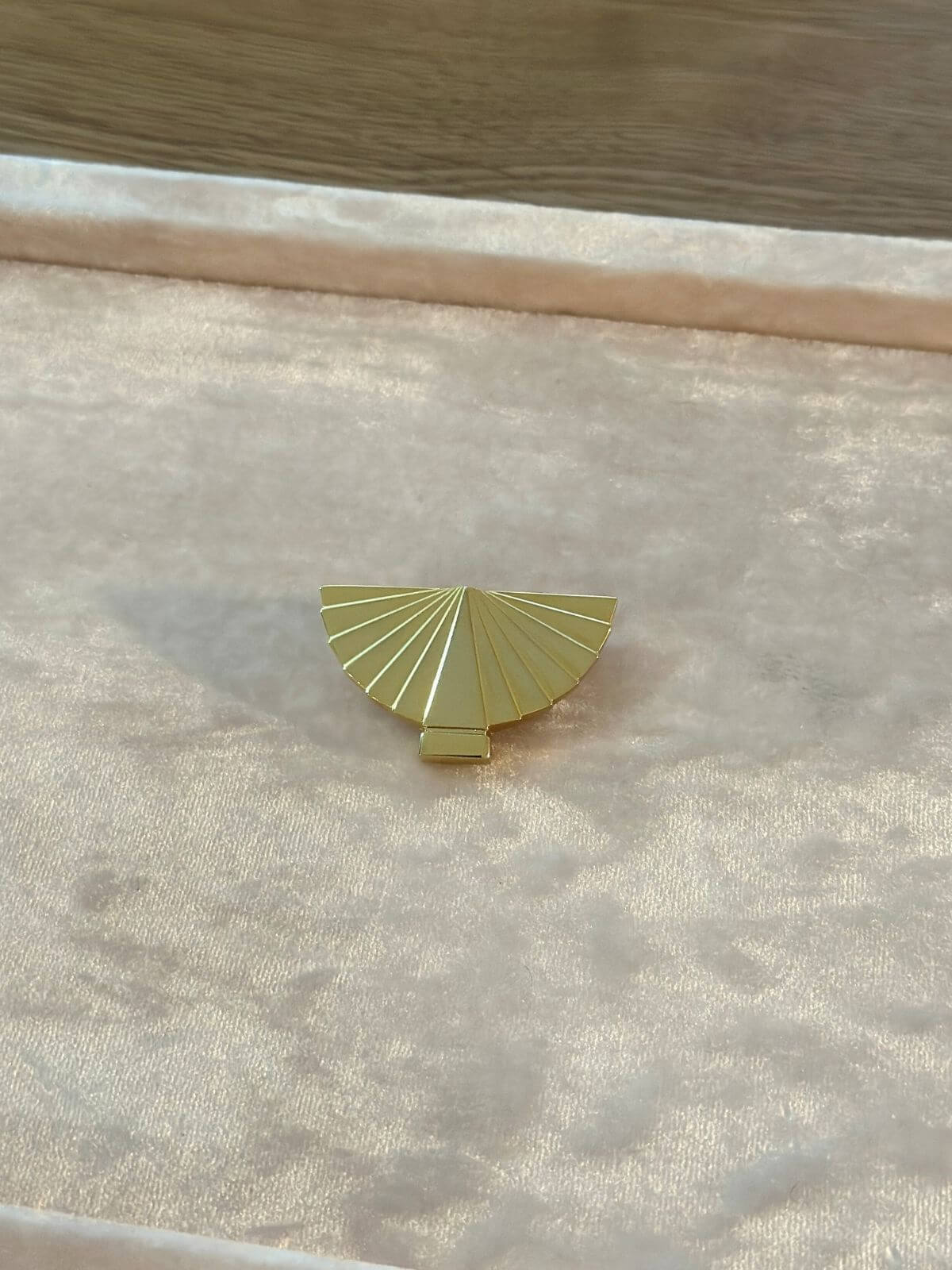 Louise Row Studio vintage Karl Lagerfeld gold fan brooch  on a textured beige surface