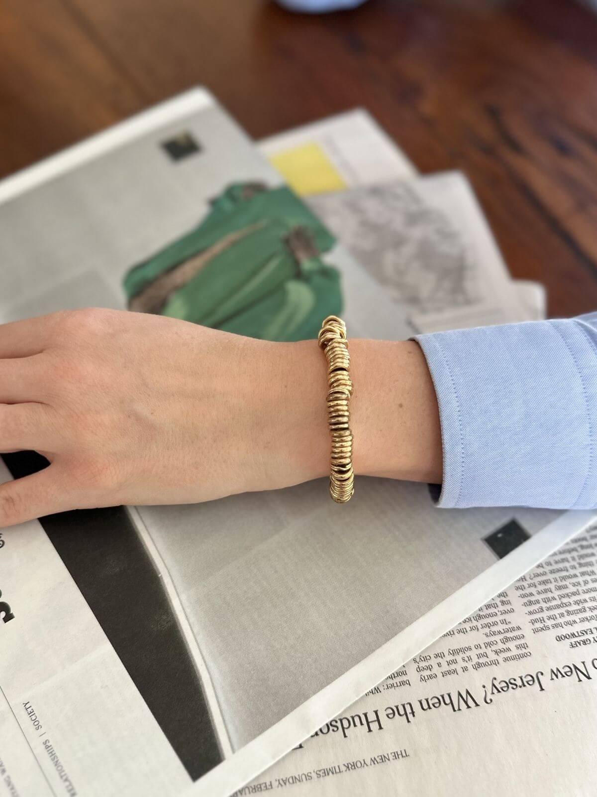 Hand wearing a gold bracelet on a surface with a blurred background