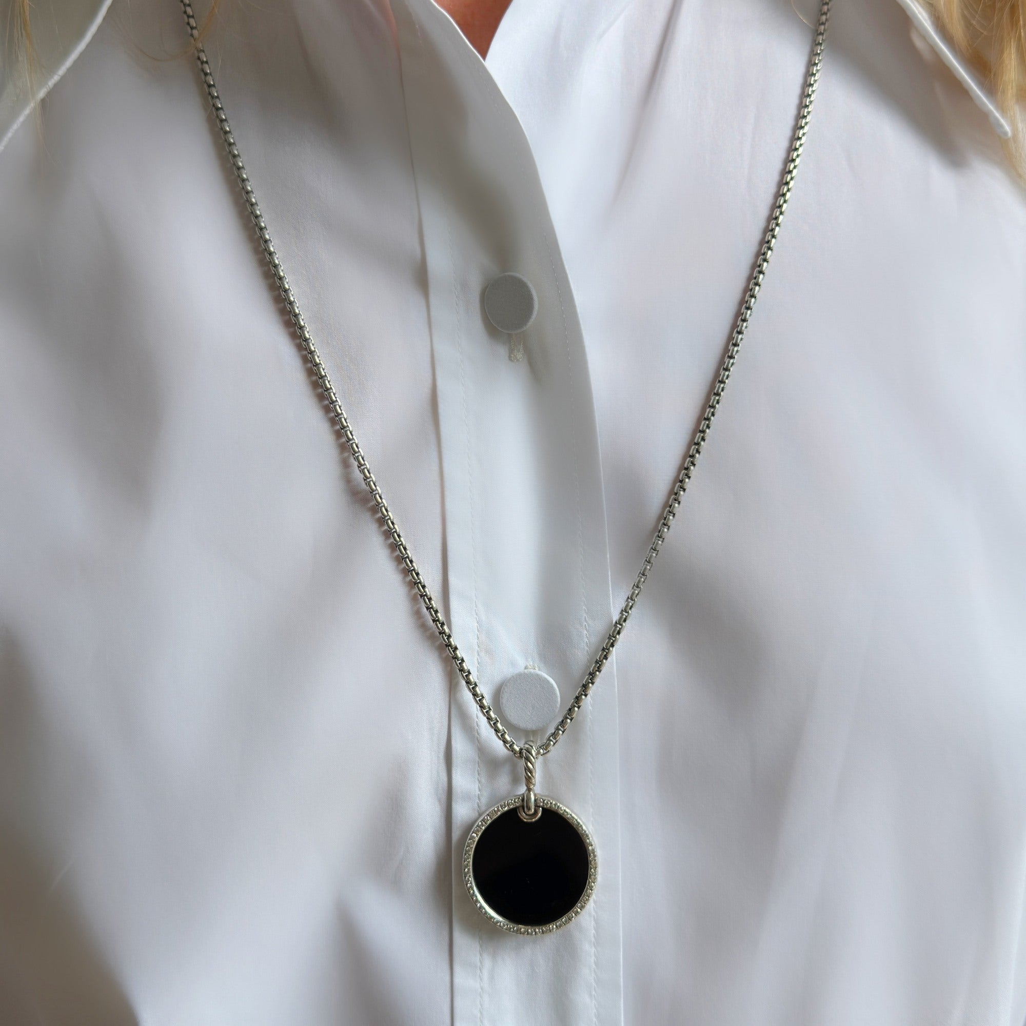 Louise Row featuring model wearing white shirt modeling a silver necklace with blank onyx pendant. 