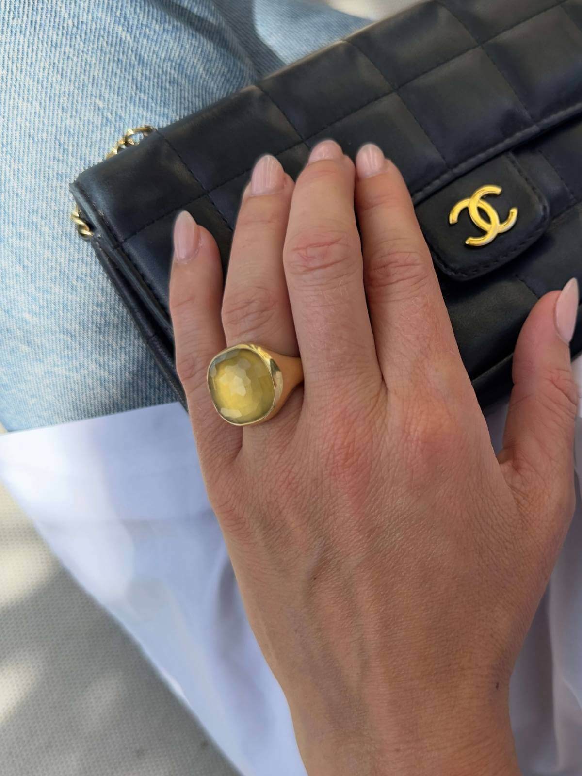 Hand with a gold ring holding a black quilted handbag with a gold clasp.