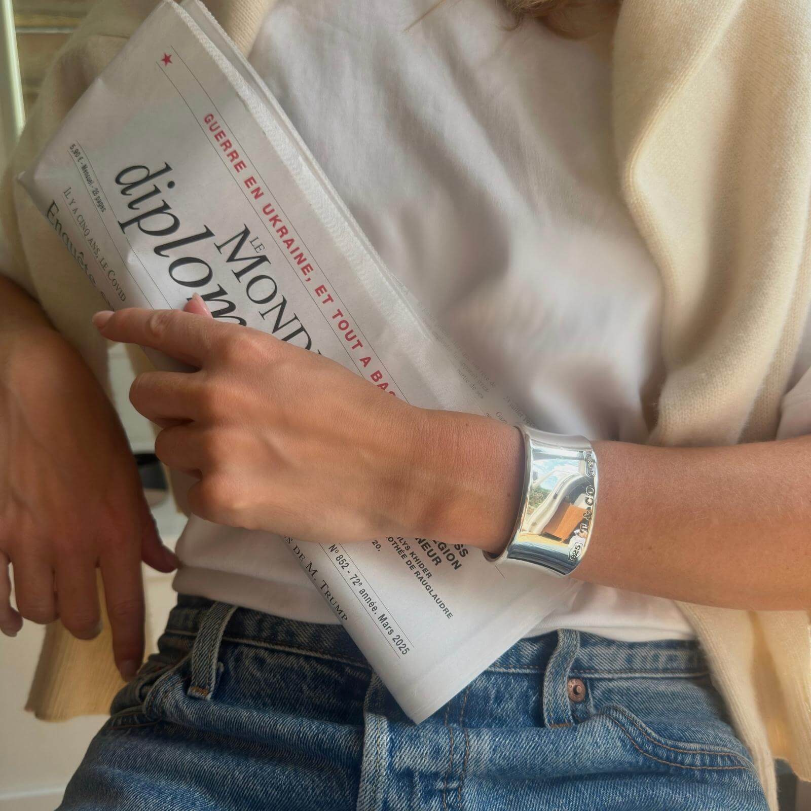 Person holding a newspaper with a focus on a hand wearing a silver bracelet.