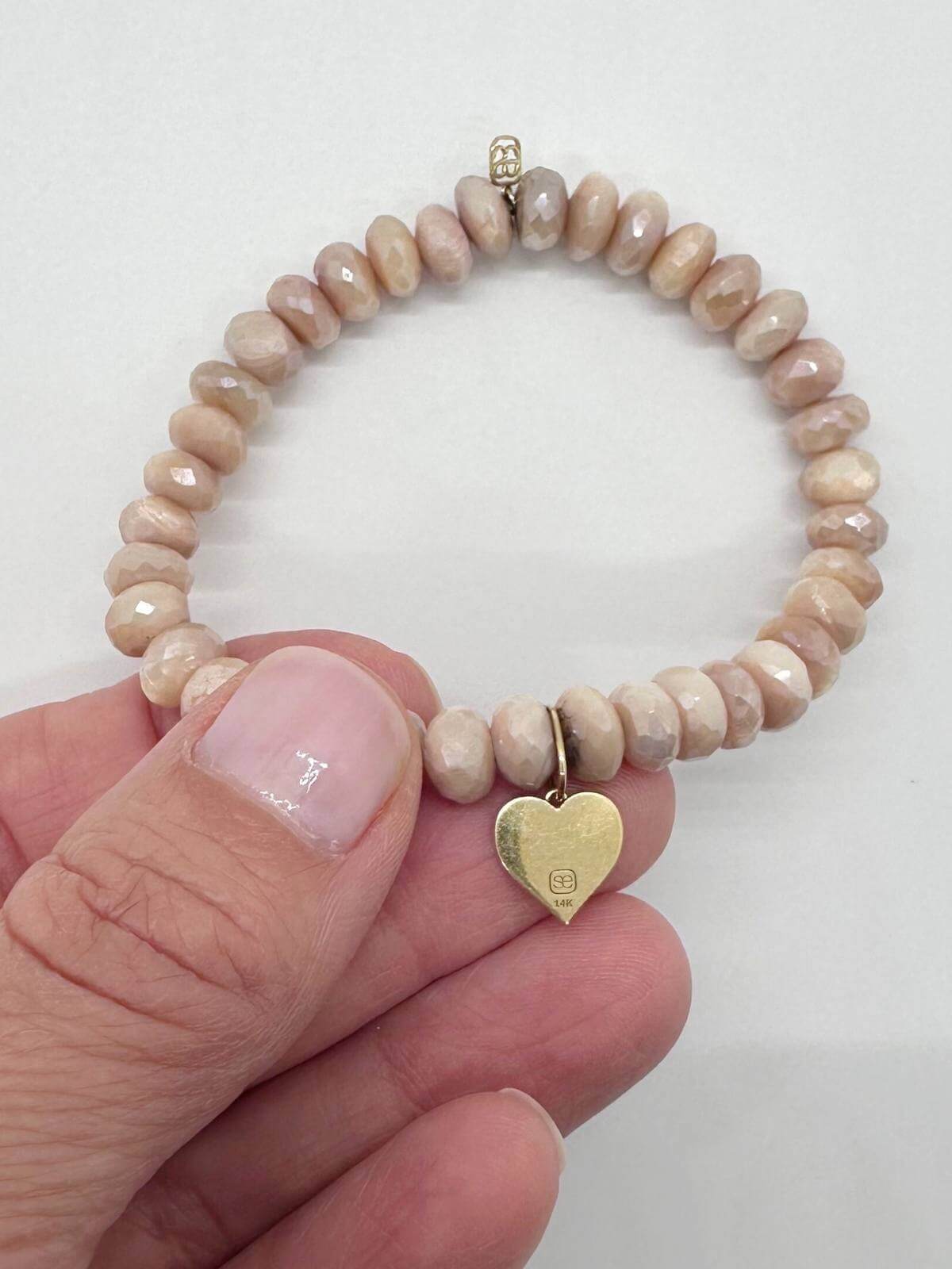 Beaded bracelet with a gold heart charm held by a hand on a white background