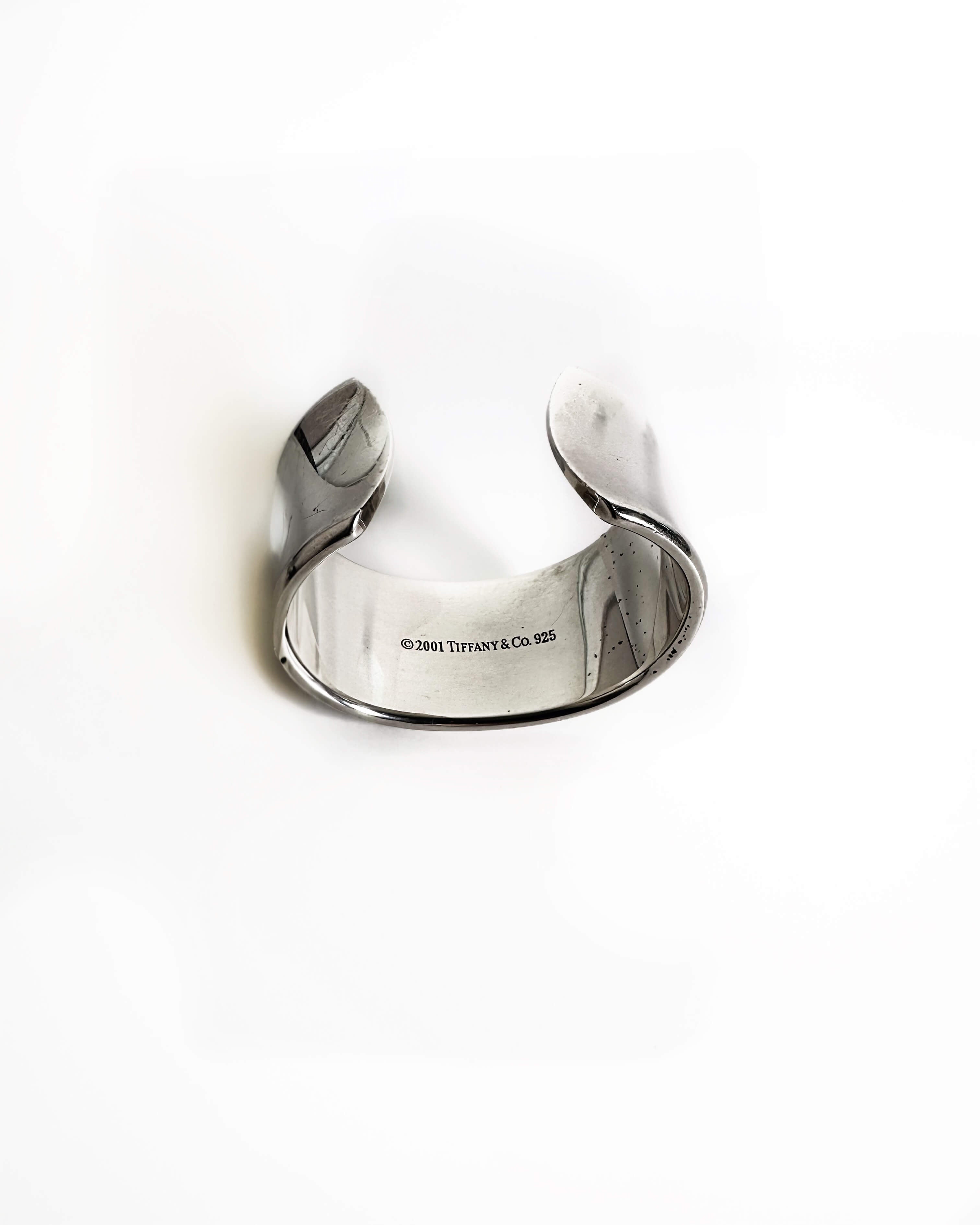 Silver cuff bracelet with 'T & Co' engraving on a white background, showing back of cuff with signature