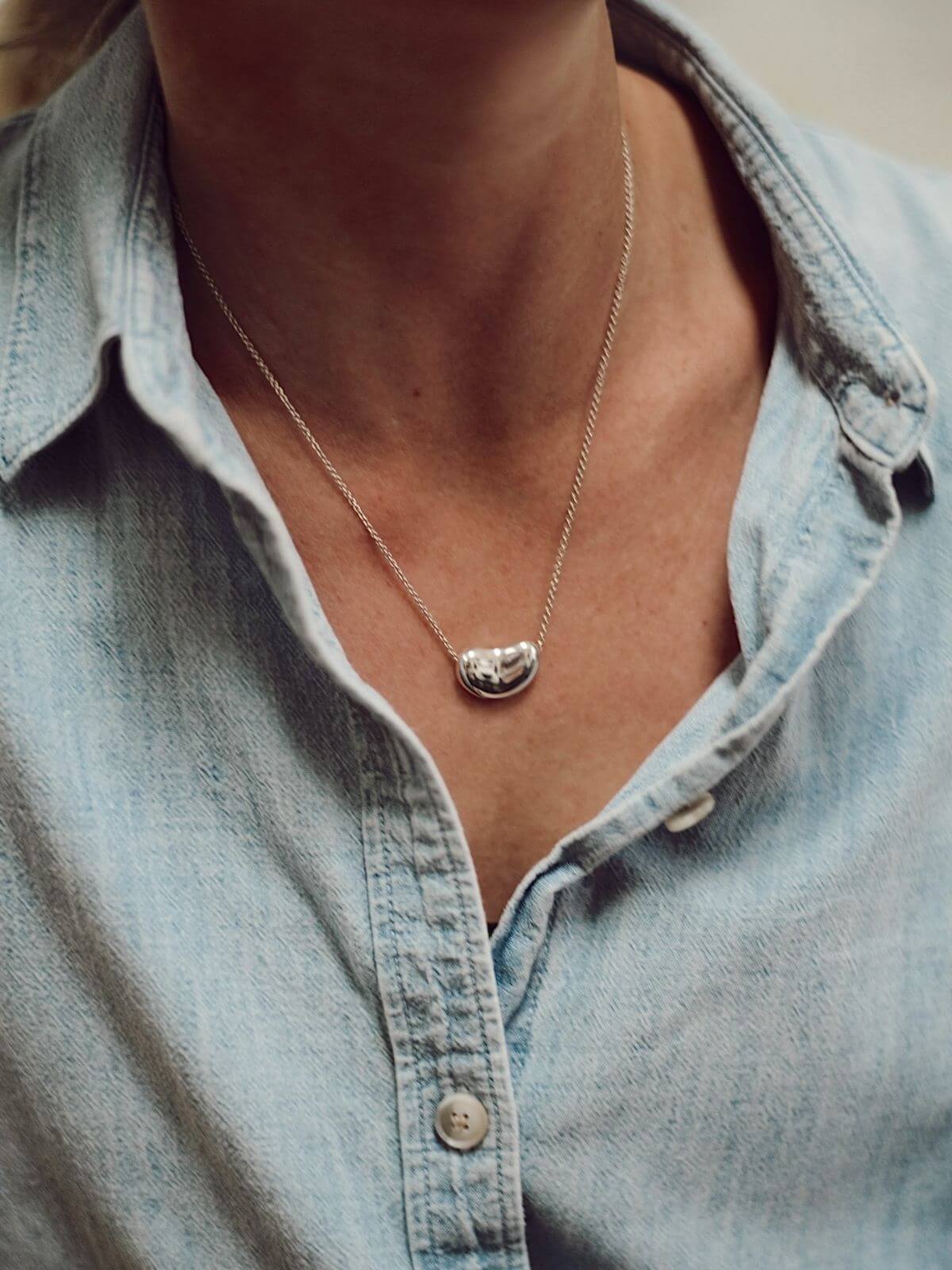Necklace with a pendant worn by a person wearing a light blue denim shirt.