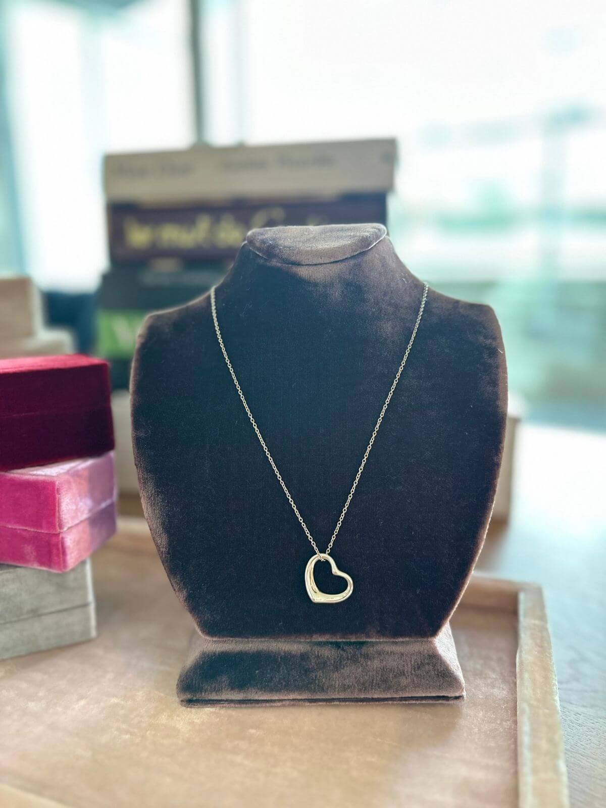 Gold heart-shaped necklace on a black velvet stand with blurred background