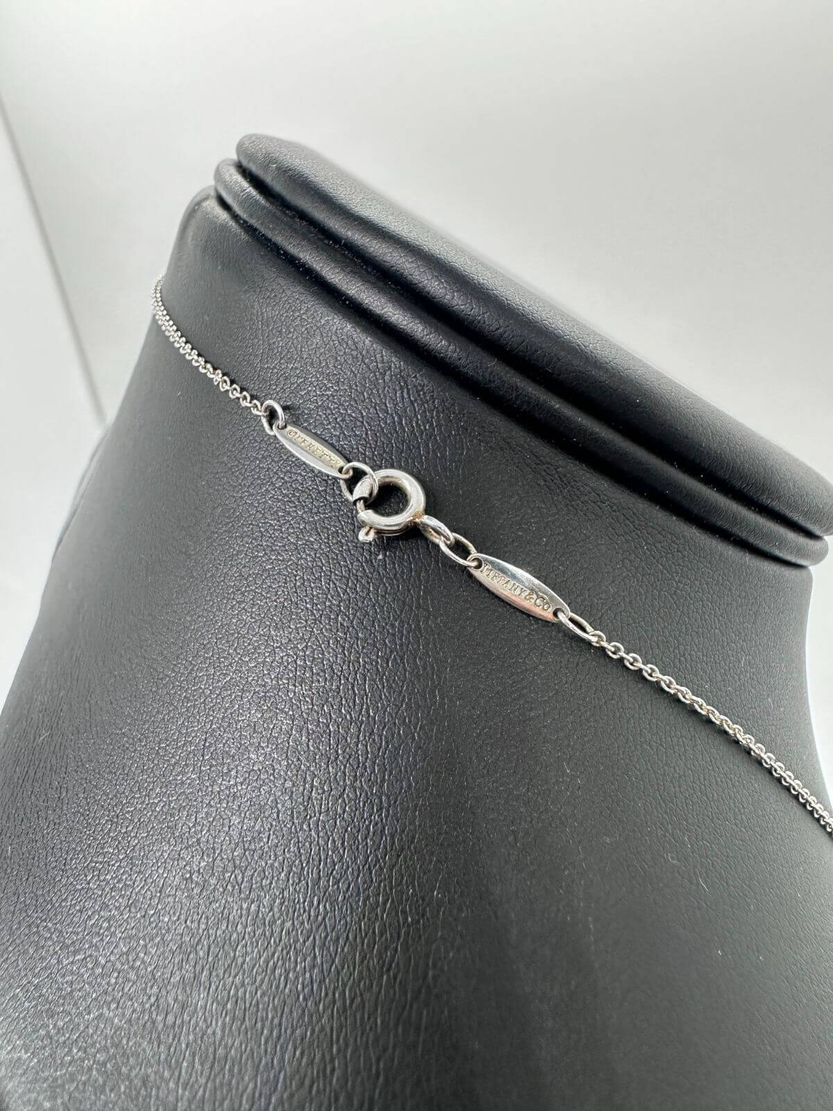 Silver Tiffany & Co solitaire diamond pendant on black fixture. Showing the signature on the back of the necklace. 