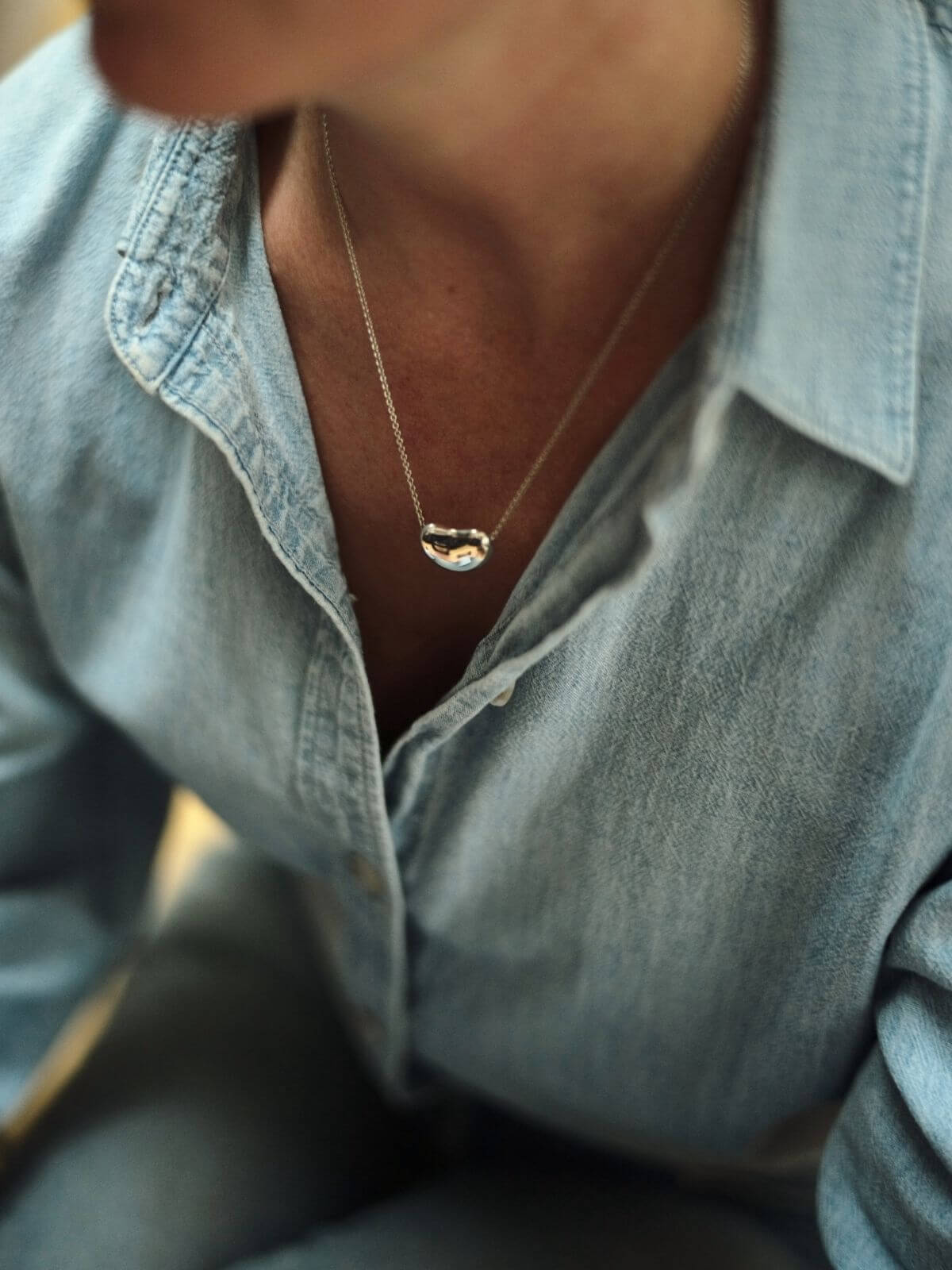 Necklace with a pendant worn by a person wearing a light blue shirt.