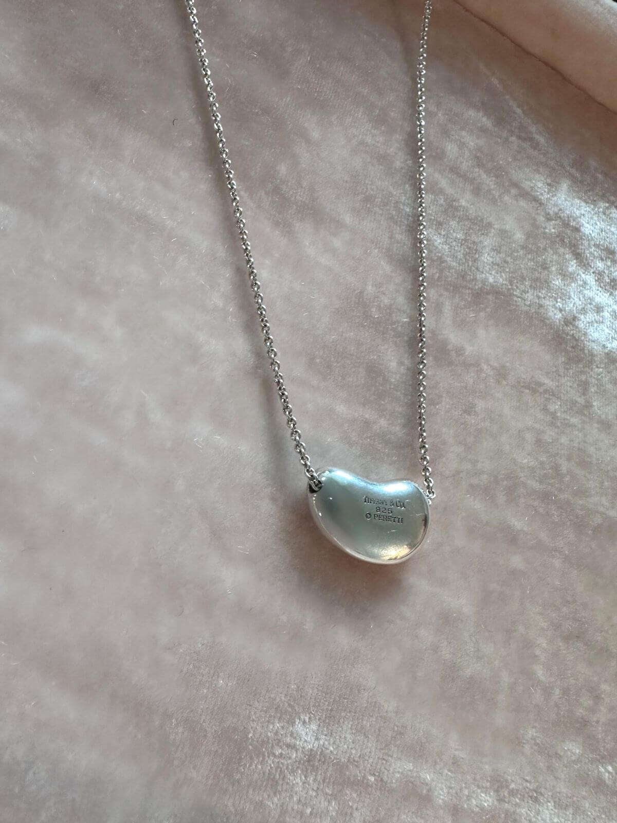 Silver necklace with a bean-shaped pendant on a light pink fabric background