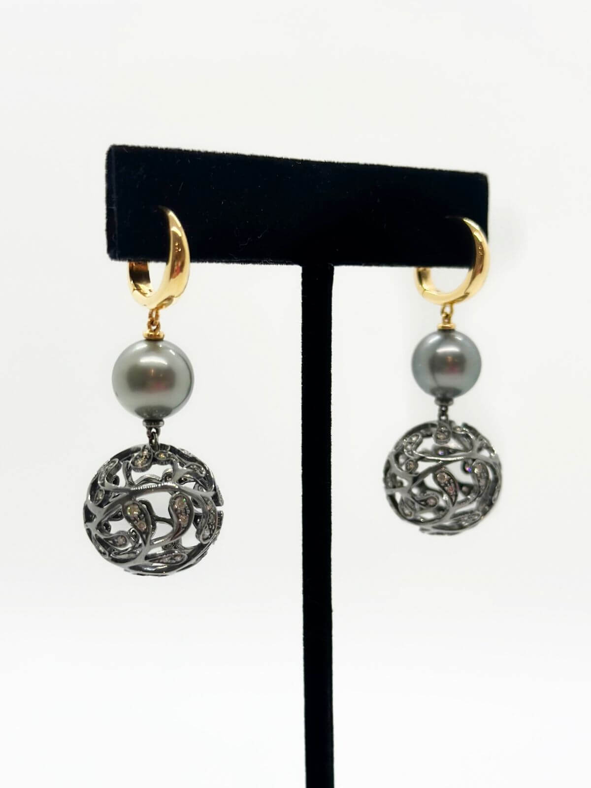 Pair of earrings with Tahitian pearls and intricate designs on a black stand against a white background