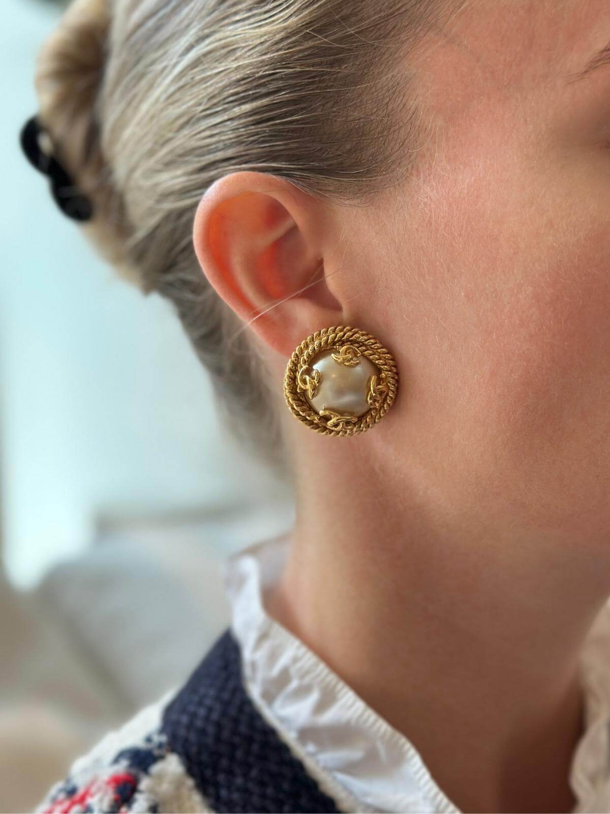 Model close-up wearing vintage Chanel pearl and gold clip on earrings.