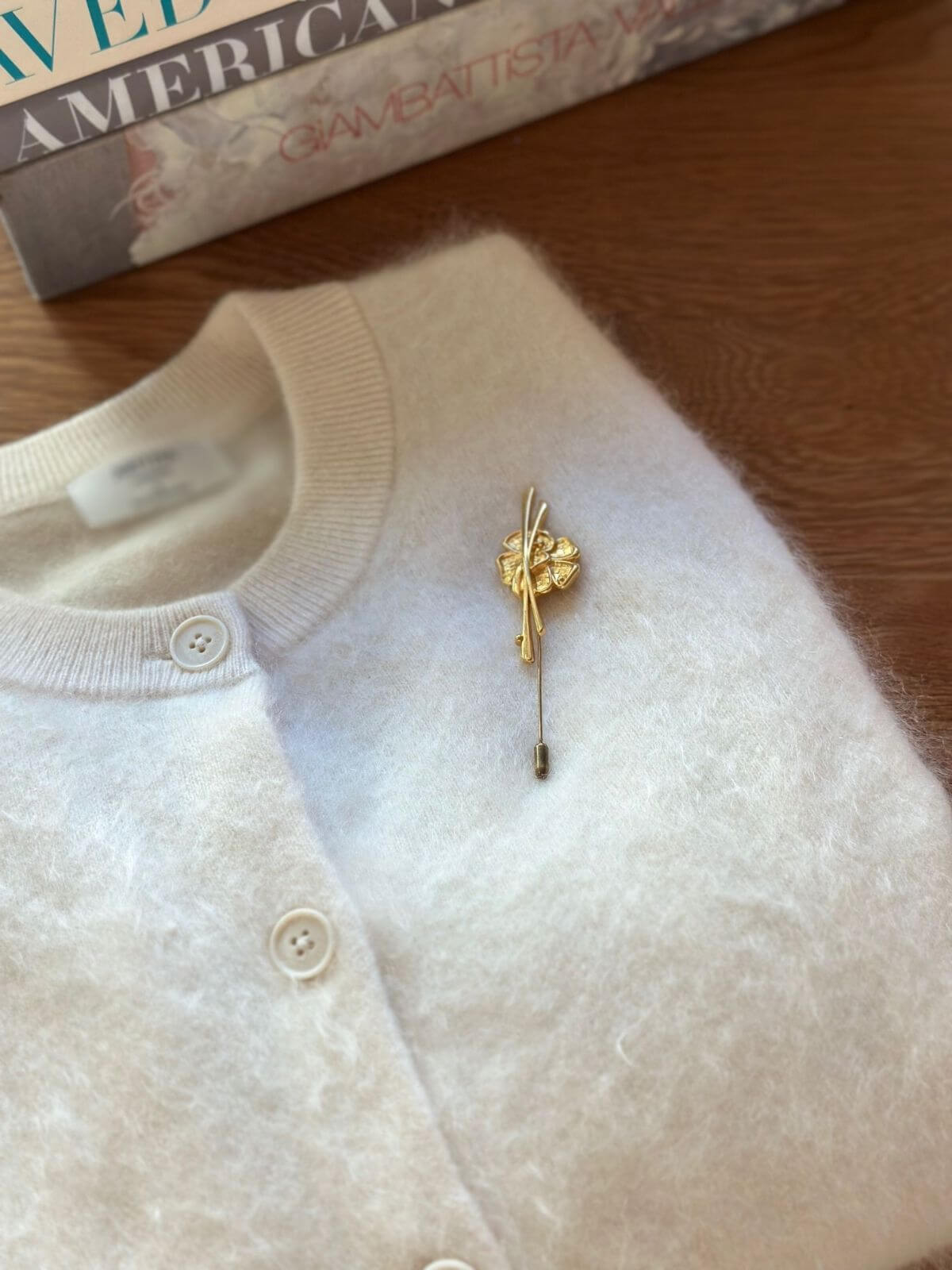 Louise Row Studio vintage Van Cleef & Arpels gold pin brooch on folded white cardigan. 