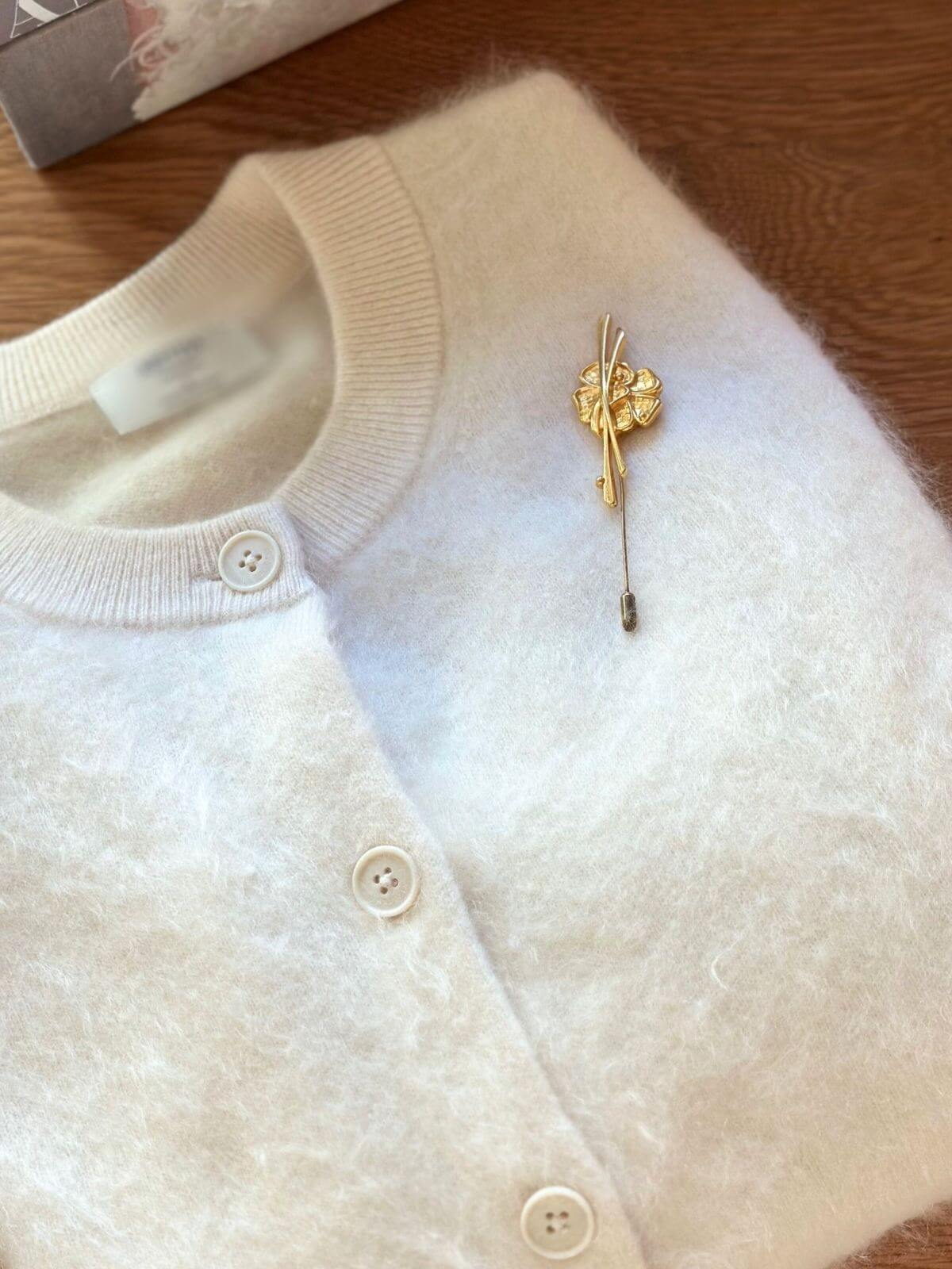 Louise Row Studio vintage Van Cleef & Arpels gold pin brooch on folded white cardigan. 