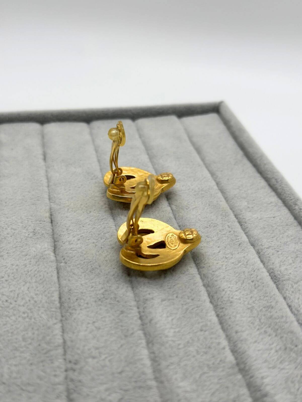 Chanel gold clip on heart earring on grey fixture. showing clip on back.