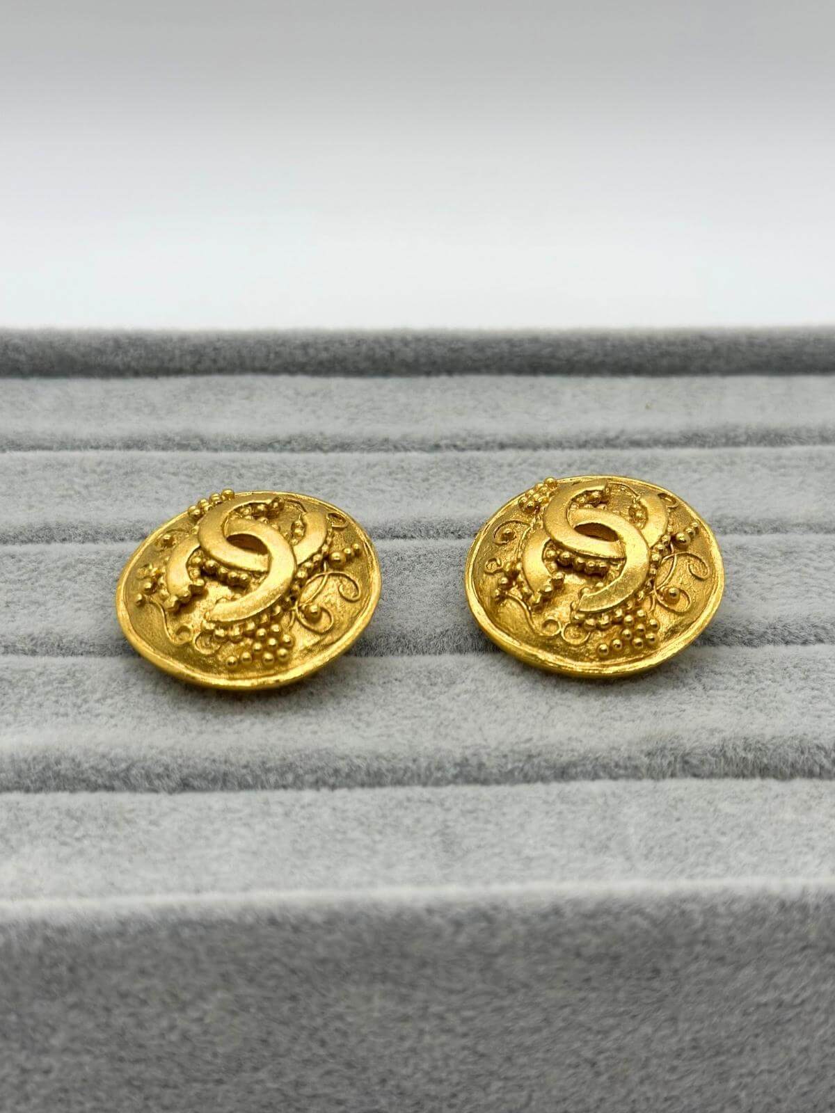 Vintage Chanel gold round earring with CC logo in center on grey background. 