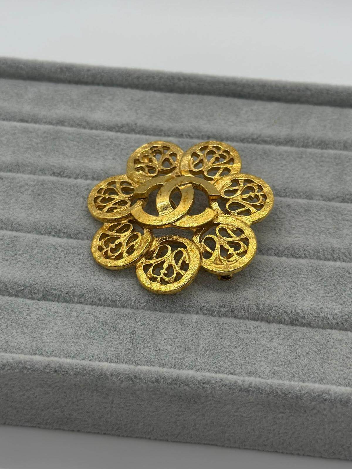 Vintage Chanel Gold sphere brooch on a grey fabric background