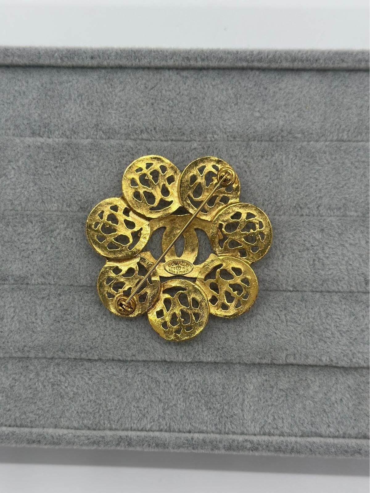 Vintage Chanel Gold sphere brooch on a grey fabric background showing back pin closure