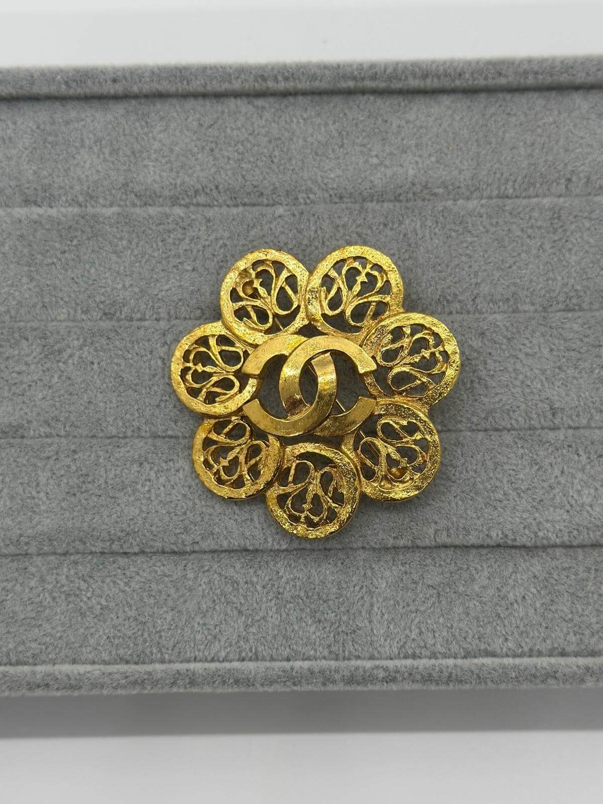 Vintage Chanel Gold sphere brooch on a grey fabric background