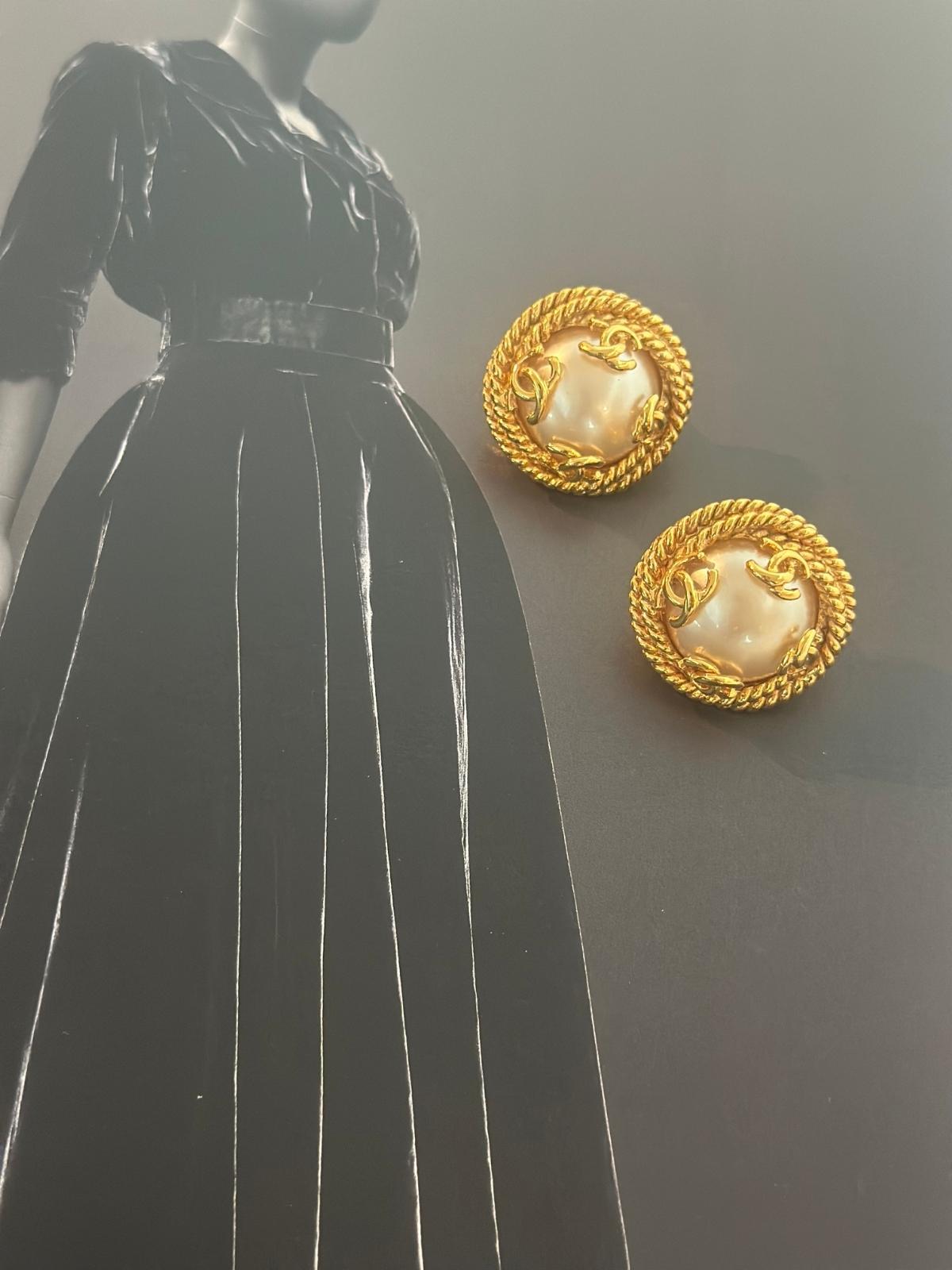 Chanel Gold earrings with pearl center displayed on a mannequin wearing a black dress.