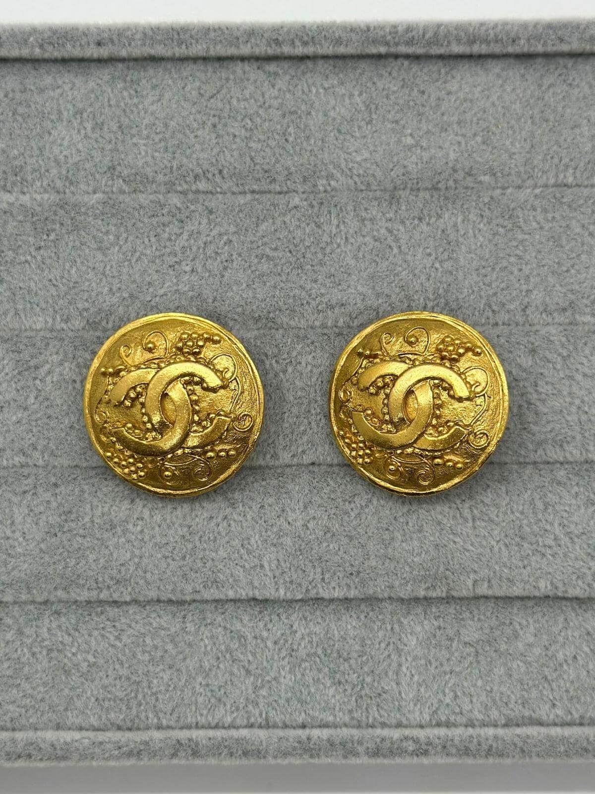 Vintage Chanel gold round earring with CC logo in center on grey background. 
