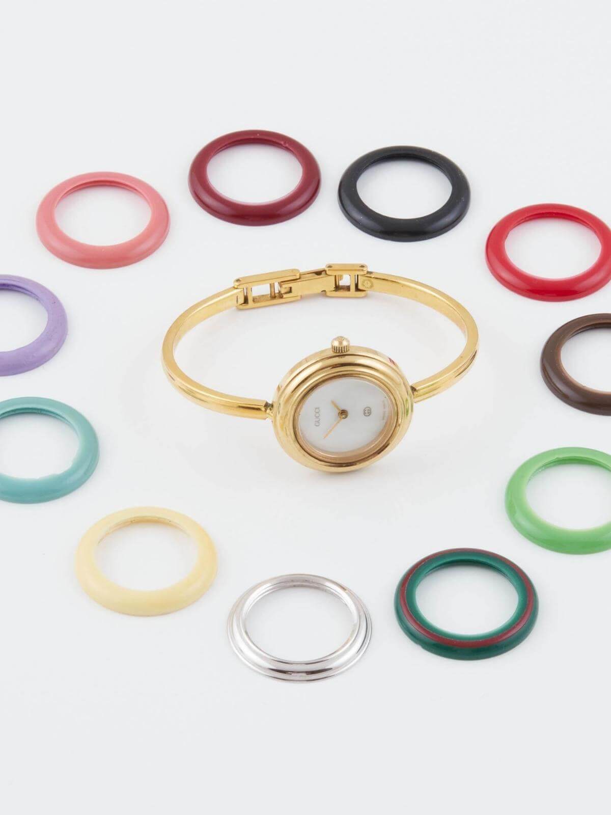 Vintage Gold Gucci  watch with colorful band options on a light gray background