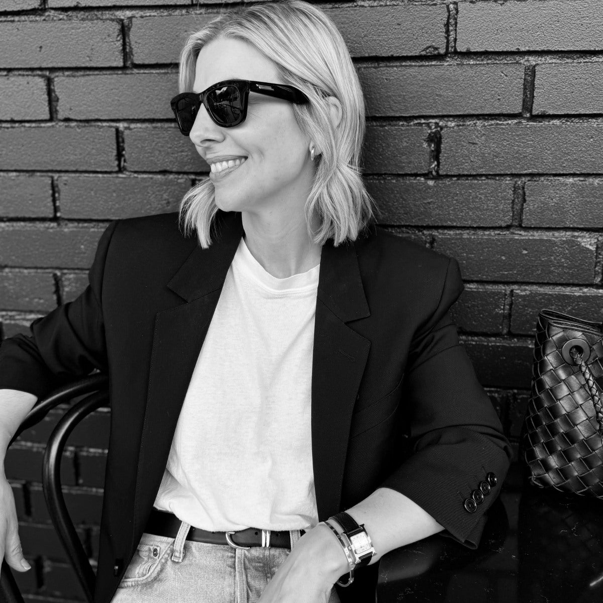 Louise Row featuring founder KimEli Krake sitting on chair and smiling wearing sunglasses. 